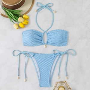 Light blue textured two-piece bikini set with shell charms and straw hat on marble background
