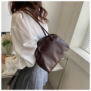 Detail of a minimalist dark brown leather tote bag carried on a shoulder for daily commute