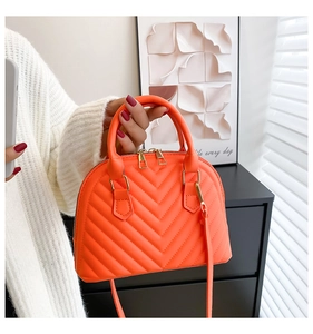 Detail of bright orange quilted shell bag with gold hardware held by a model