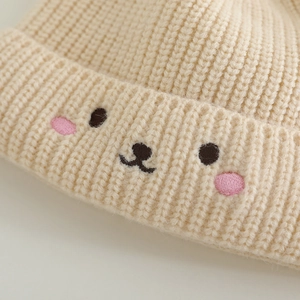 Knitted bear baby hat with cute animal embroidery and dual pom-poms in beige