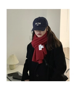 Detail shot of a red chunky knit scarf paired with a navy New York embroidered cap