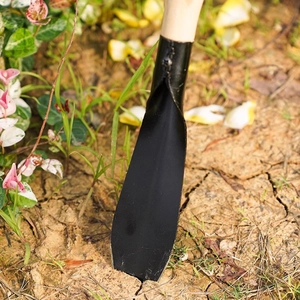Garden shovel with black manganese steel blade and wooden handle digging in soil
