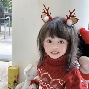 Close-up of a child wearing plush reindeer antler headbands with festive red decorations
