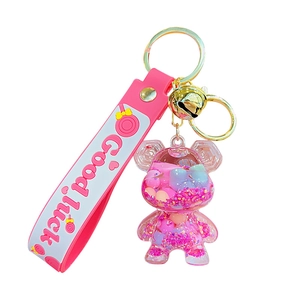 Pink bear liquid quicksand keychain with Good Luck strap and gold bell on white background