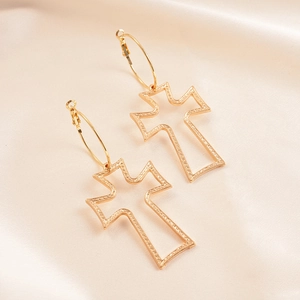 Detail of gold hollowed-out cross earrings displayed on an elegant beige silk fabric background