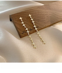 Detail of long gold star tassel earrings with zircons on elegant champagne silk