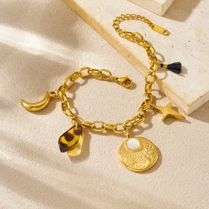 Gold celestial charm bracelet with moon, sun disc, and tassel on a beige stone base