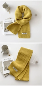 Close-up of ginger yellow chunky knit scarf featuring a white woven label on white background