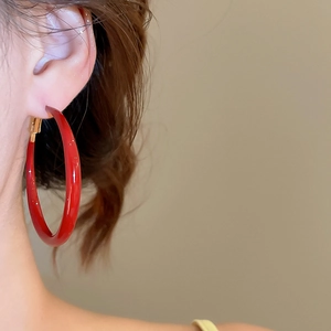 Close-up of a large red hoop earring with high-gloss finish worn on the earlobe