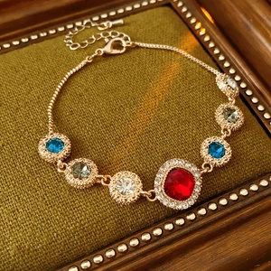 Close-up of vintage gold bracelet with colorful crystals on dark wood and green fabric