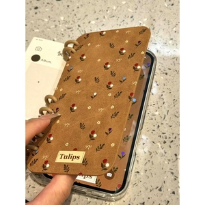 Brown floral iPhone case with tulip pattern and spiral binding design in a hand