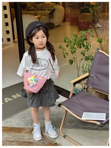 Kids pink woven crossbody bag with pearl flower charms worn by a young model outdoors