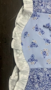 Detailaufnahme von blauem Blumenstoff mit elegantem weißen Spitzenbesatz am Oberteil