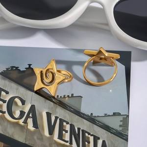 Détail d'une bague étoile dorée ouverte posée sur un fond de magazine de mode chic
