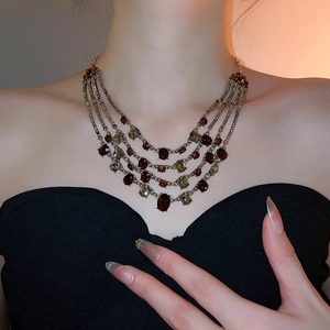 Macro shot of layered gold necklace with dark red gems on a model in black dress