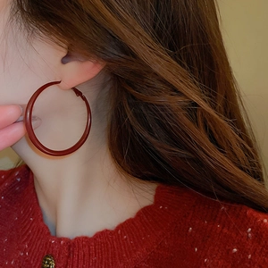 Close-up of a model wearing large dark red geometric hoop earrings with a glossy finish