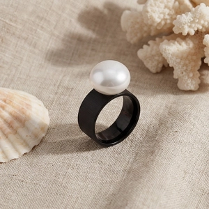 Detail of wide black matte ring with large white pearl on textured linen with shells