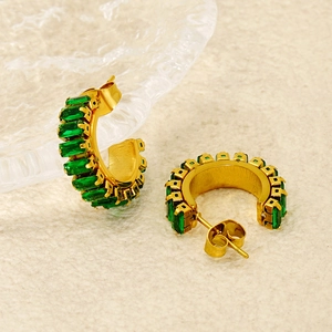 Macro shot of gold C-shaped earrings with baguette-cut emerald zircon stones