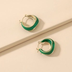 Detail of green enamel geometric earrings with golden borders on a soft beige background