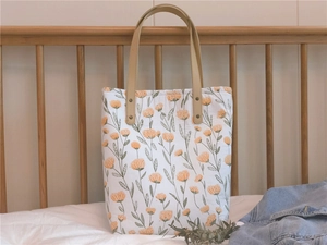 Gros plan d'un sac cabas fleuri matelassé avec des poignées en cuir beige et rivets