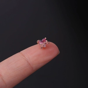 Detailed macro of a gold heart-shaped pink zircon ear stud held on a fingertip