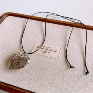Retro engraved heart pendant necklace with black wax rope cord on a linen display tray