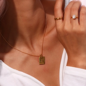 Detail shot of a 18K gold plated necklace with engraved rectangle pendant and matching ring