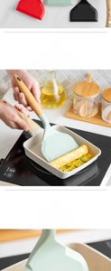 Silicone tamagoyaki spatula with beech wood handle flipping eggs in a non-stick pan
