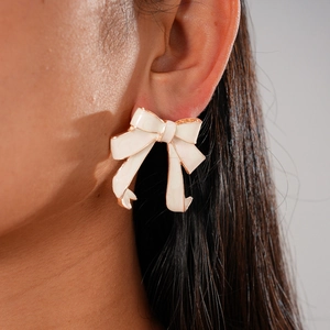 Close-up of white enamel bow earring with rose gold trim on model's ear
