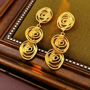 Close-up of golden vintage swirl earrings on green velvet pad in a wooden frame