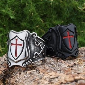Vintage stainless steel cross shield rings in silver and black on natural bark background