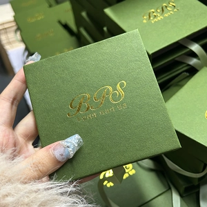 Detalle del joyero verde oscuro con textura de tela y logotipo dorado estampado