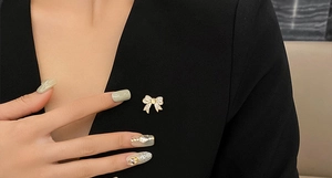 Détail macro d'une broche nœud dorée ornée de zircons blancs sur un revers de veste noir