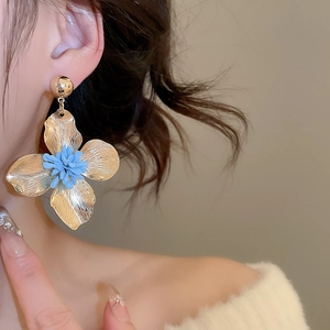 Detail of golden metal flower earrings with blue stamen on model for premium look