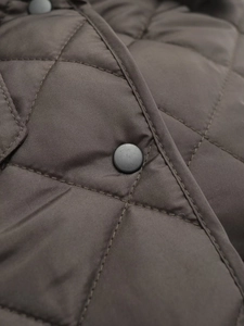Macro shot of diamond quilting and matte black snap button on oversized jacket