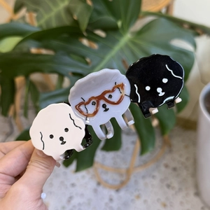 Three cute puppy hair claws in black, white, and grey acetate material set against greenery