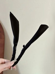 Dettaglio di un fermaglio per capelli in raso nero a forma di fiocco tenuto in mano