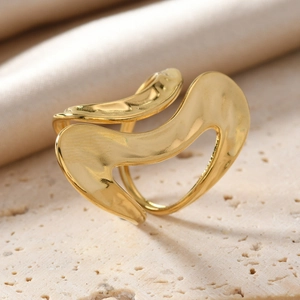 Macro detail of golden irregular wavy ring on stone surface with satin fabric backdrop