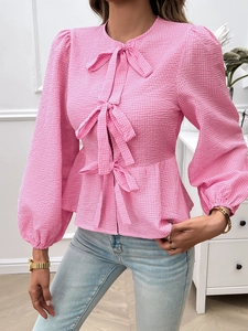 Detail of pink plaid blouse featuring front bow ties, puff sleeves, and ruffle hem