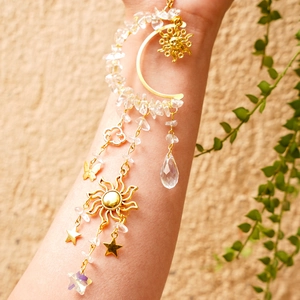 Detail of moon and sun suncatcher with natural crystals held on a person's wrist