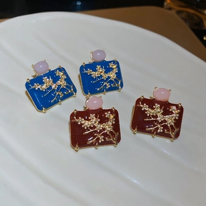 Detail of vintage enamel plum blossom earrings with gold relief on a ceramic plate