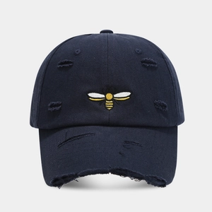 Close-up of embroidered bee and distressed ripped holes on navy blue cotton baseball cap