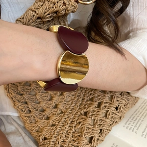 Detail of trendy gold metal and burgundy resin chunky bracelet worn with vintage accessories
