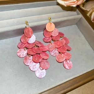 Close-up of pink layered fringe earrings with shell luster texture on a grey velvet tray