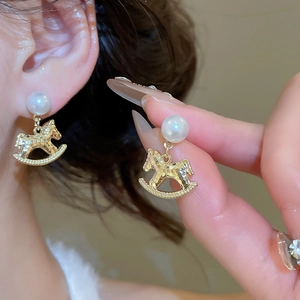 Detailed close-up of golden horse earrings with pearls and hammered metal texture
