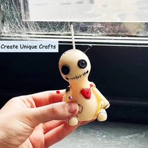 Detailed macro of a handmade voodoo doll candle with button eyes and red heart accent