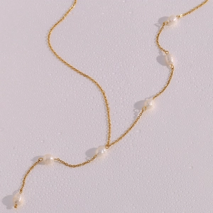 Close-up of golden stainless steel Y-chain with white freshwater pearls on a wet background