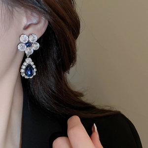 Close-up of floral silver earrings with blue and clear zircon crystals on a model