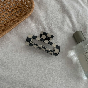 Detail of checkered acetate hair claw clip on white fabric with minimalist decor