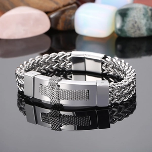 Detail of silver stainless steel woven chain bracelet with cross pattern on metal plate